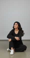 Woman in black outfit sitting on the floor against a plain background