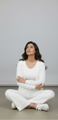 Woman in a white outfit sitting on the floor against a plain background