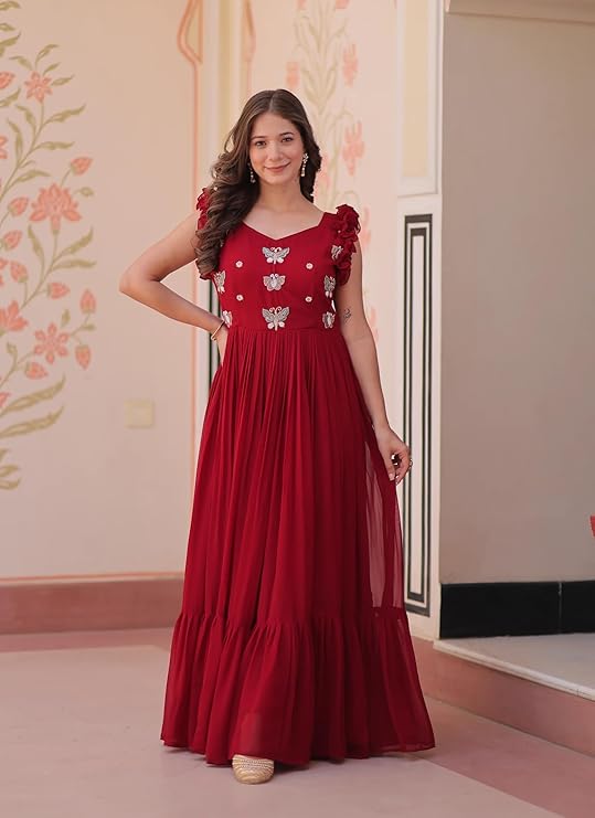 Woman wearing a red dress with floral embellishments in a room with decorative walls.