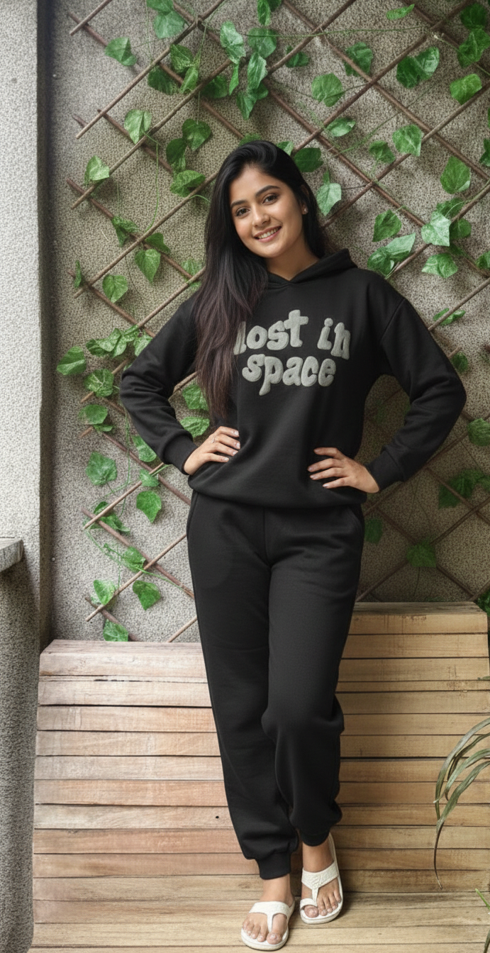 Woman wearing a black hoodie with 'Lost in Space' text, standing against a wall with greenery.