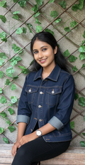 Woman wearing a denim jacket sitting against a wall with greenery