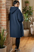 Woman wearing a navy blue hoodie in a home setting with plants and furniture.
