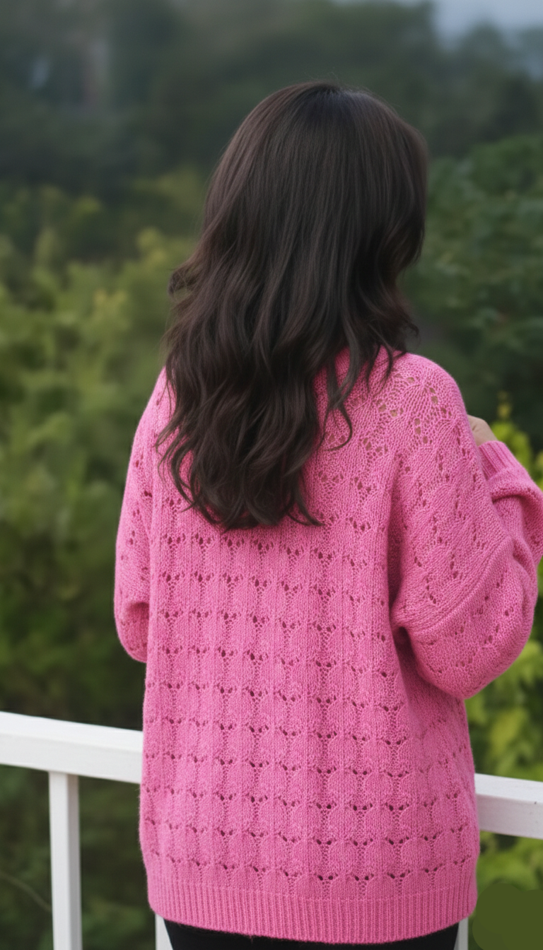 Person wearing a pink knitted sweater standing outdoors with greenery in the background