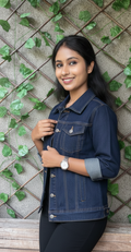 Woman wearing a denim jacket standing against a textured wall with greenery