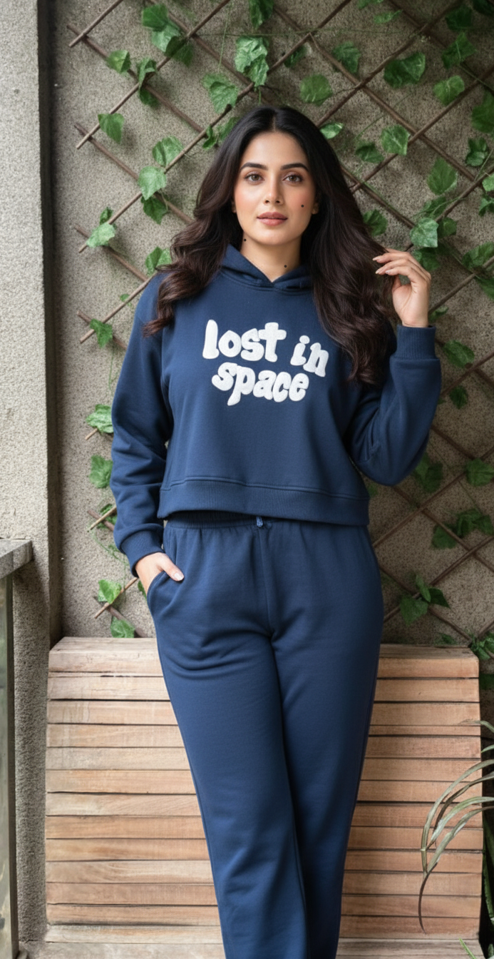 Woman wearing a blue hoodie with 'Lost in Space' text against a textured wall with greenery.