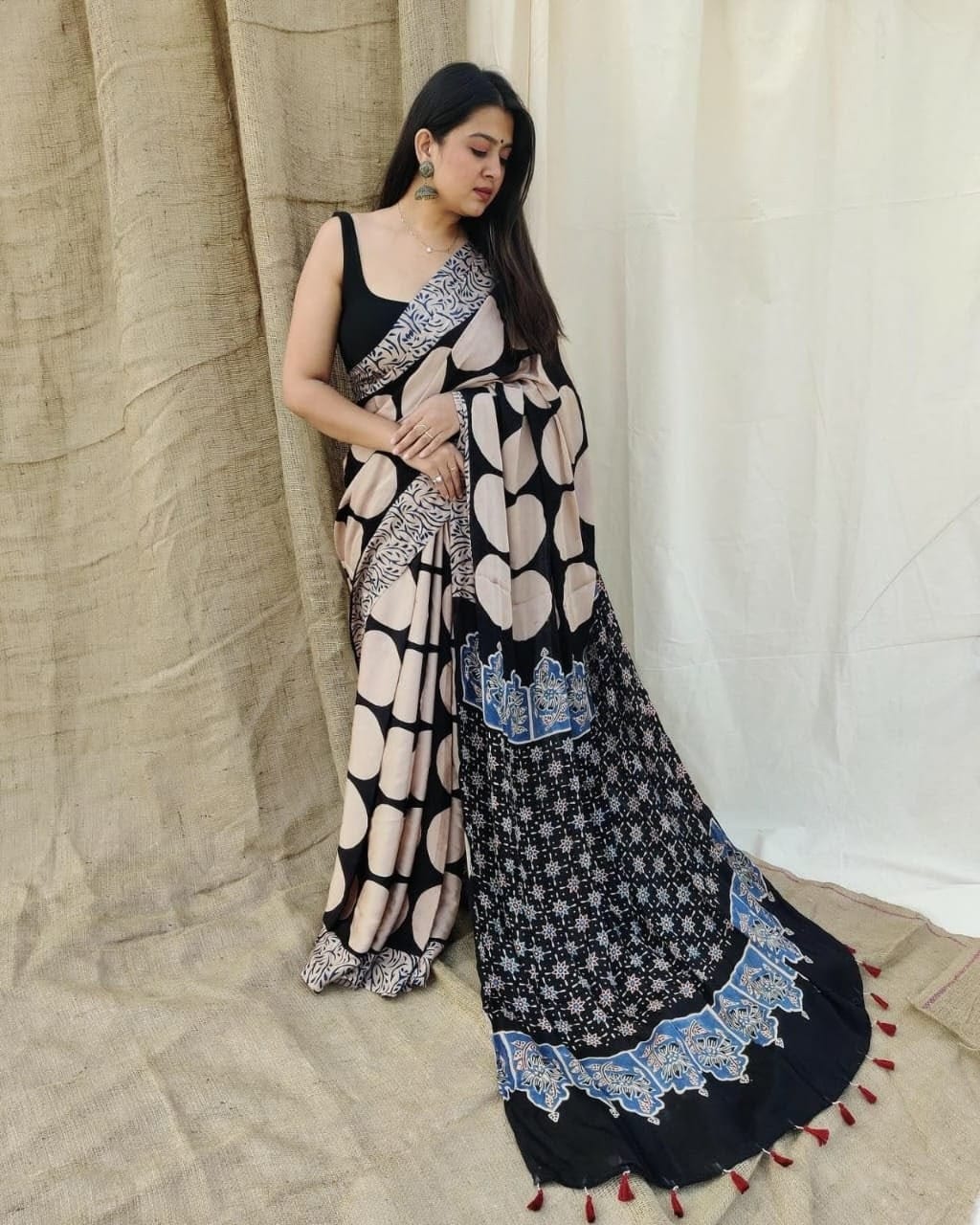 Woman wearing a black and white patterned saree with a white curtain background