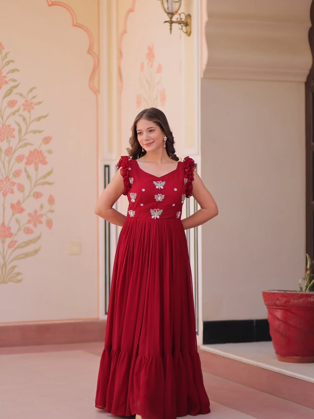 Woman in a red dress with floral patterns standing in a decorated room.