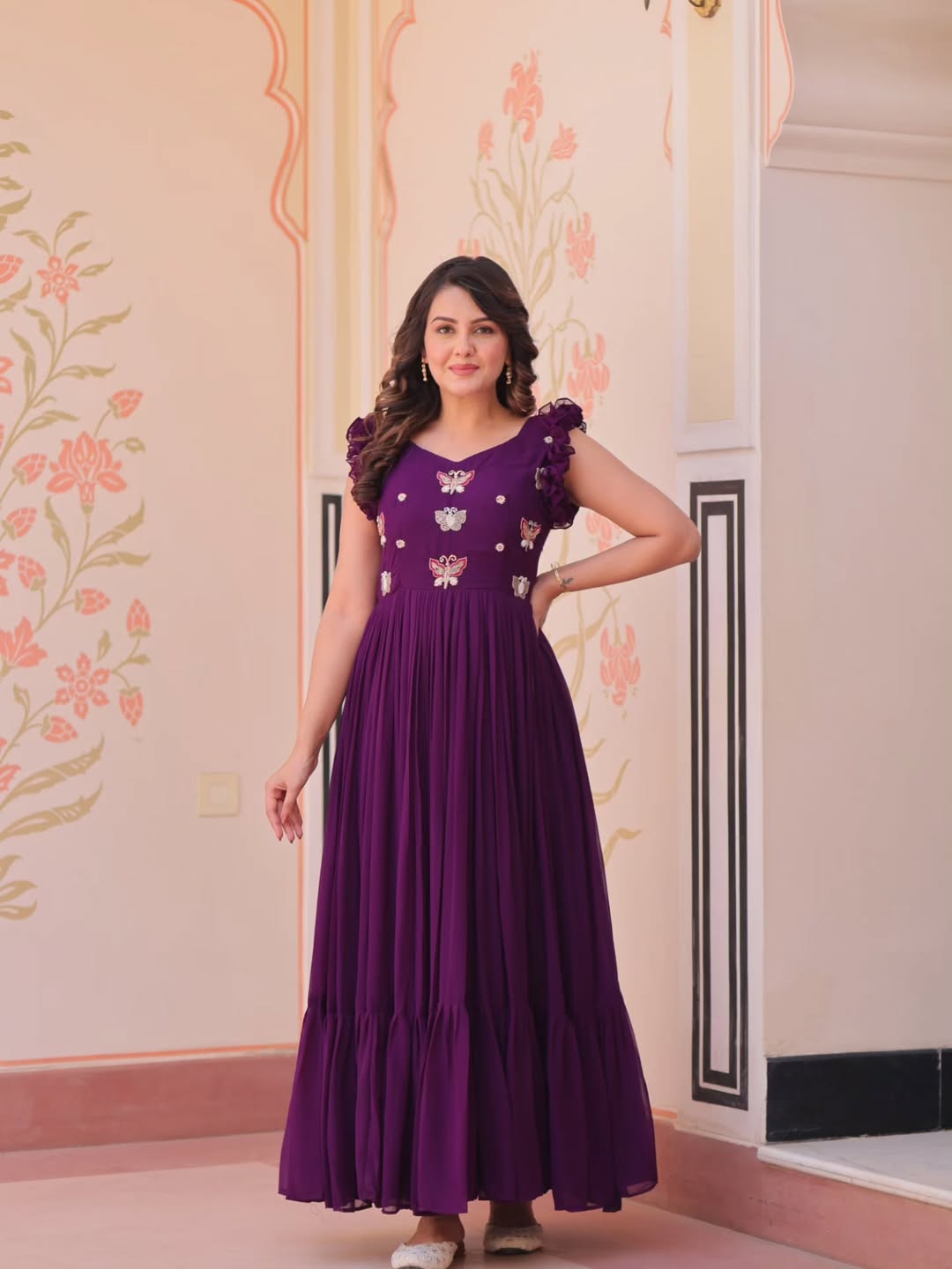 Woman wearing a purple dress with floral patterns in an indoor setting.