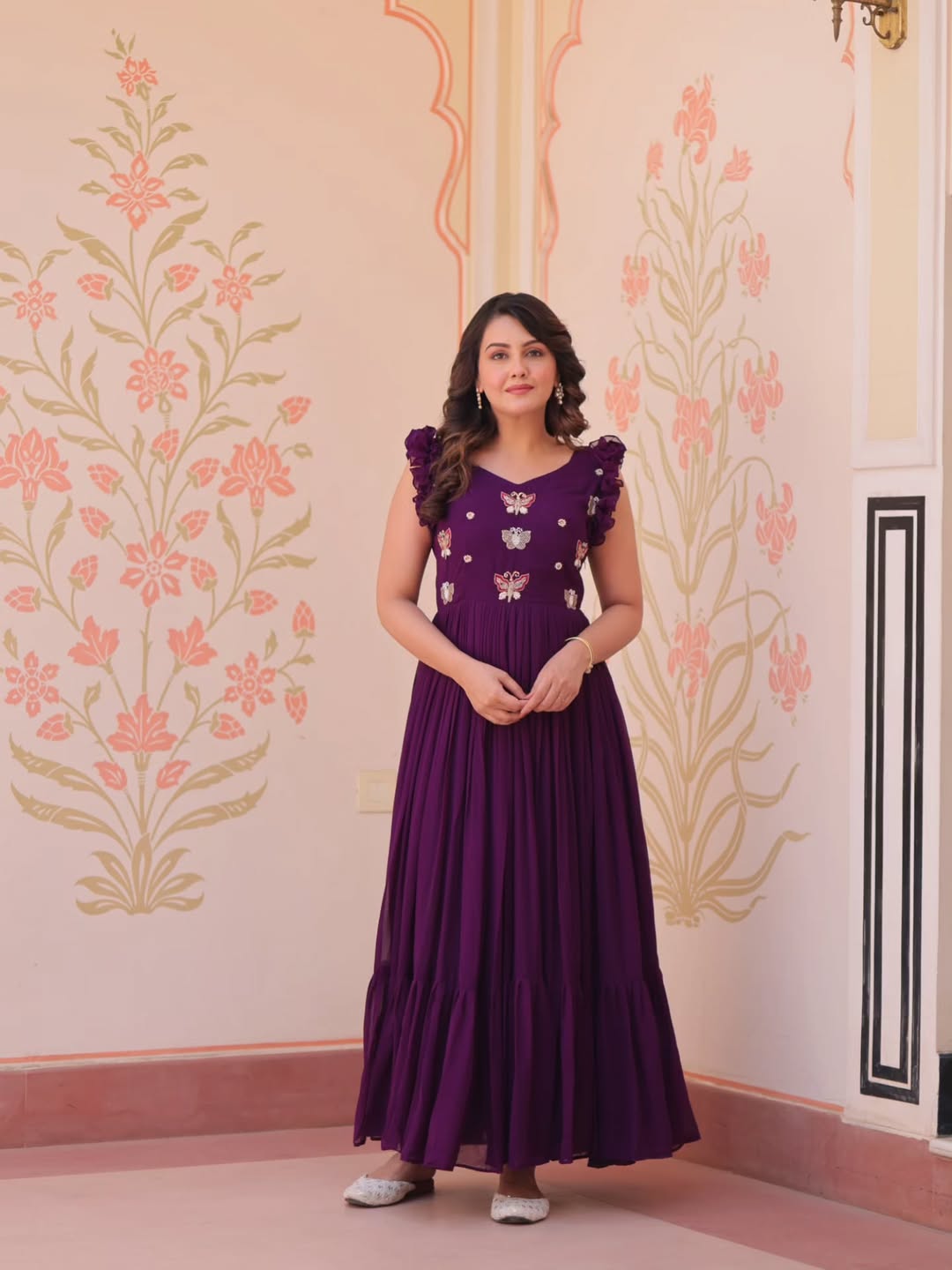 Woman in a purple dress standing against a decorated wall.