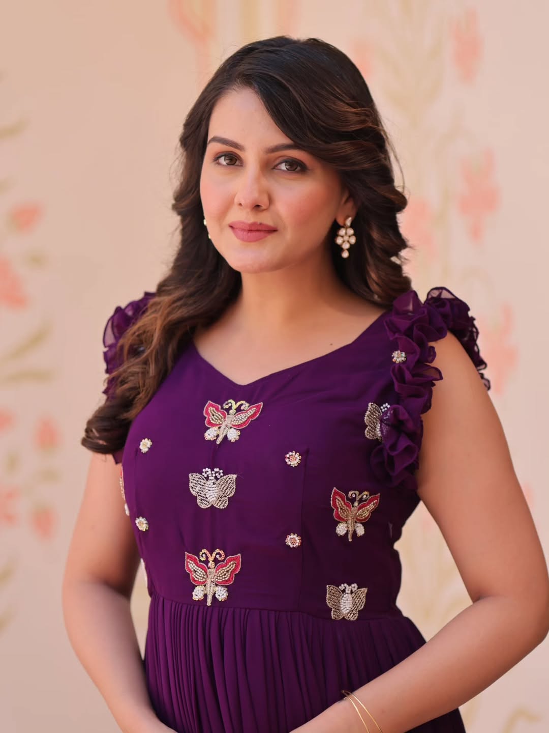 Woman wearing a purple dress with floral patterns in an indoor setting.