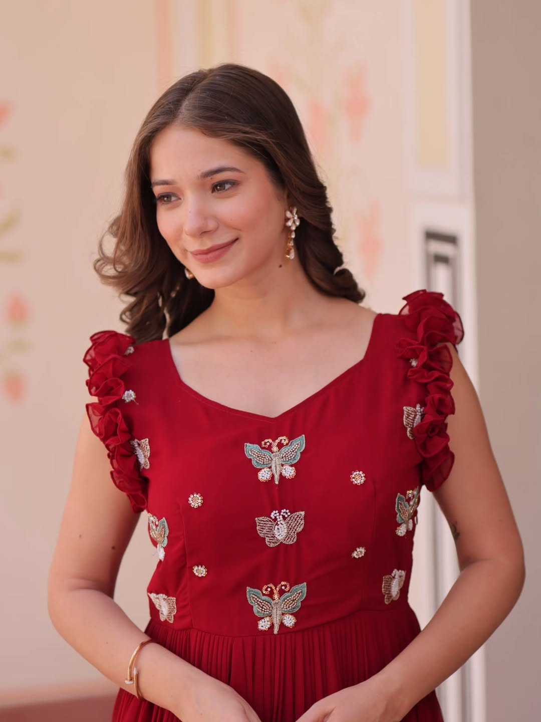 Woman in a red dress with butterfly patterns standing in a decorated room.