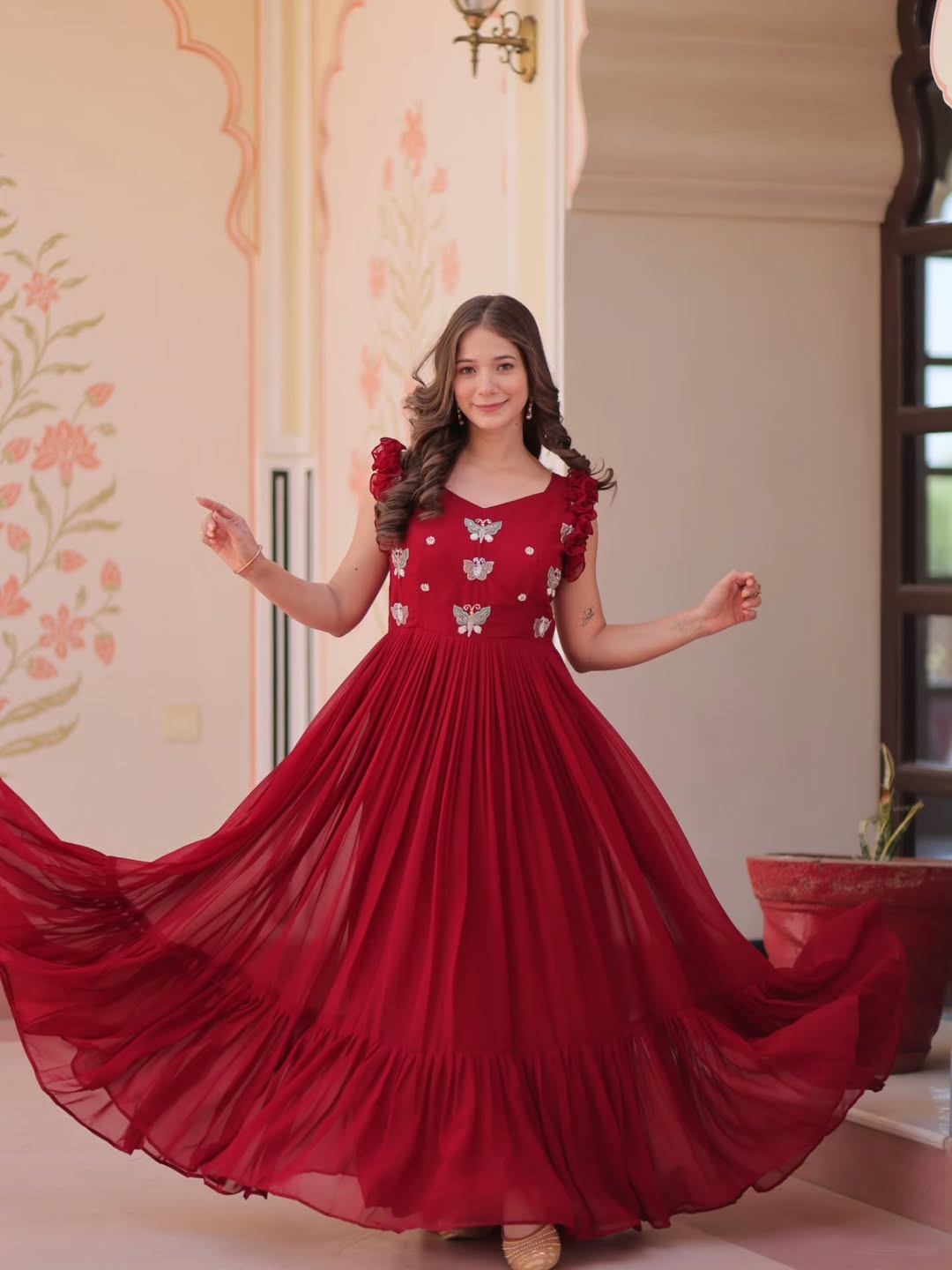 Woman in a red dress with floral patterns standing in a room with decorative walls.