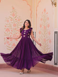 Woman in a purple dress posing in front of a decorated wall.