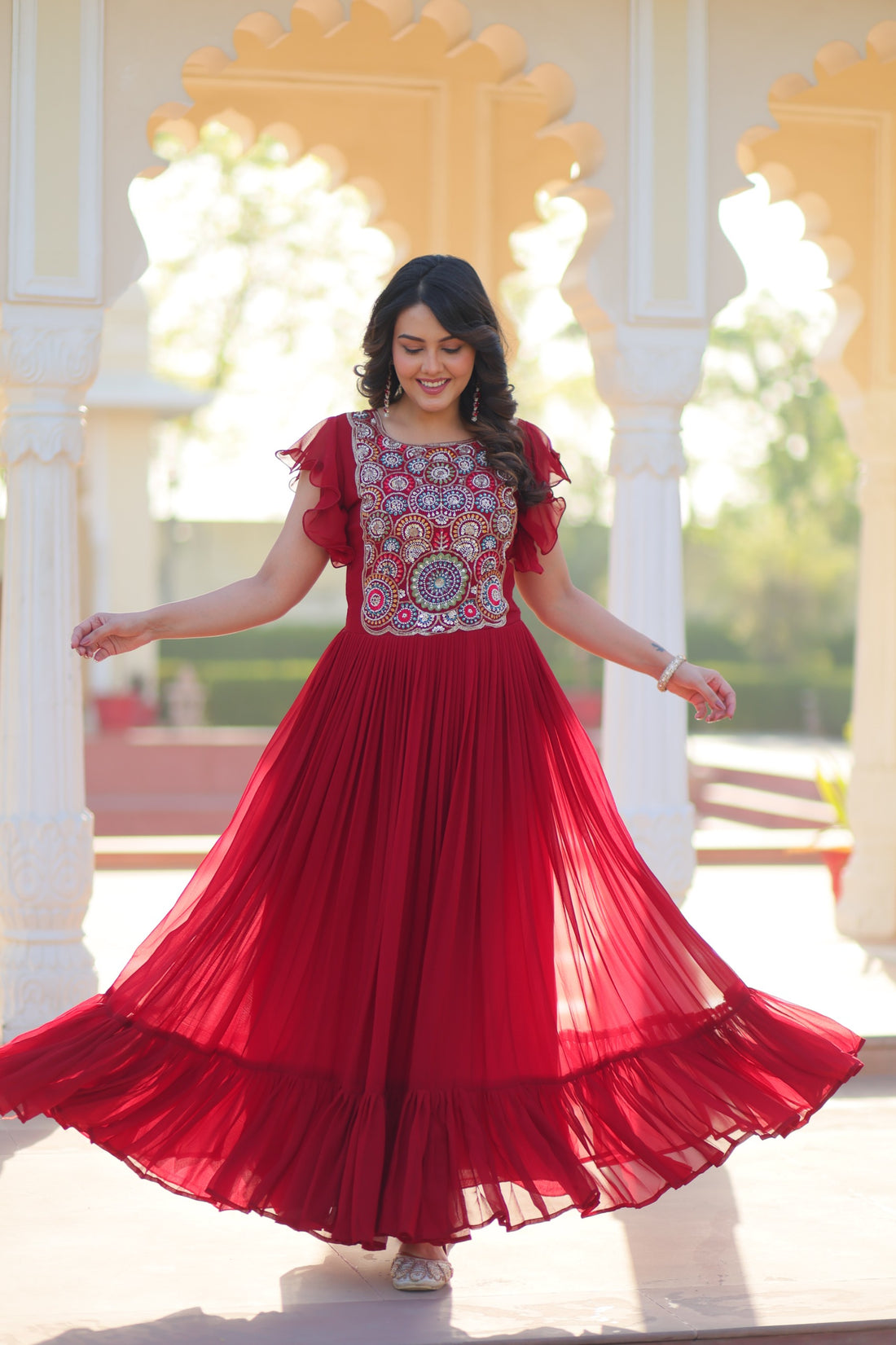 Woman in a red dress with floral patterns standing in front of an ornate architectural background.