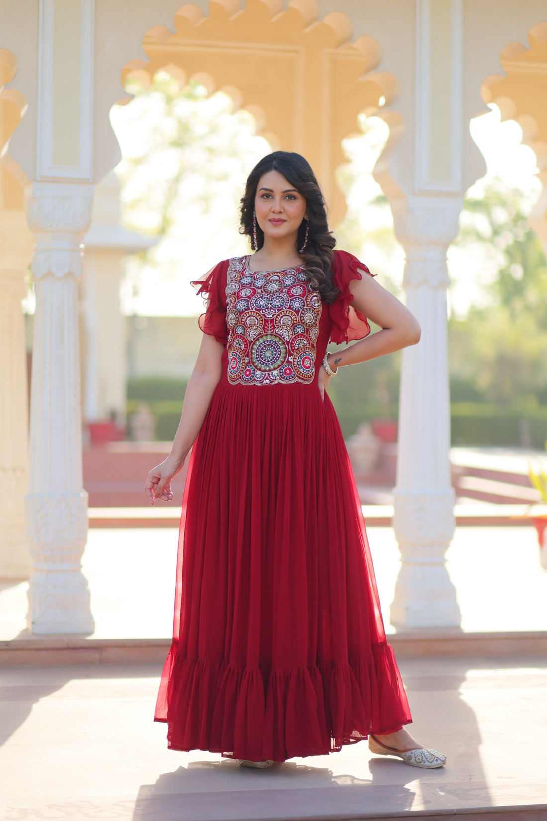 Woman in a red dress with floral patterns standing in front of an ornate architectural background.