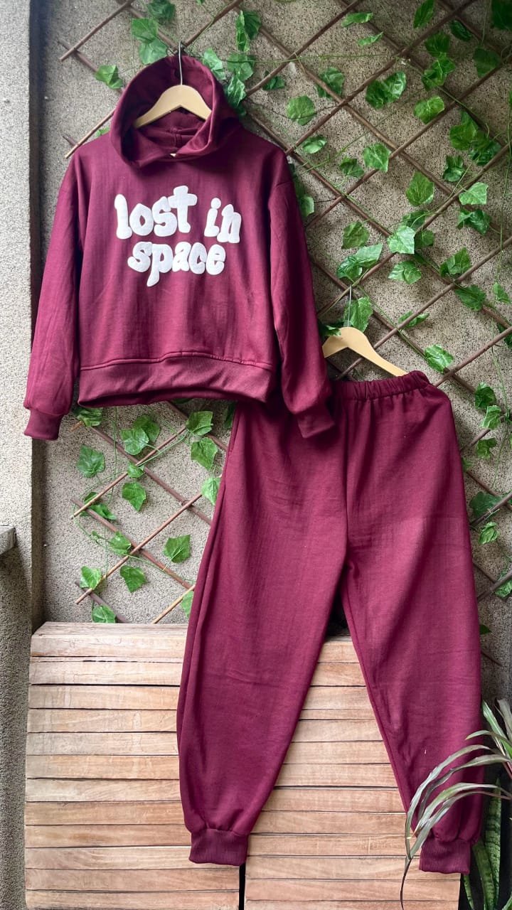 Maroon hoodie and pants set with 'Lost in Space' text on a wooden bench against a stone wall with greenery.