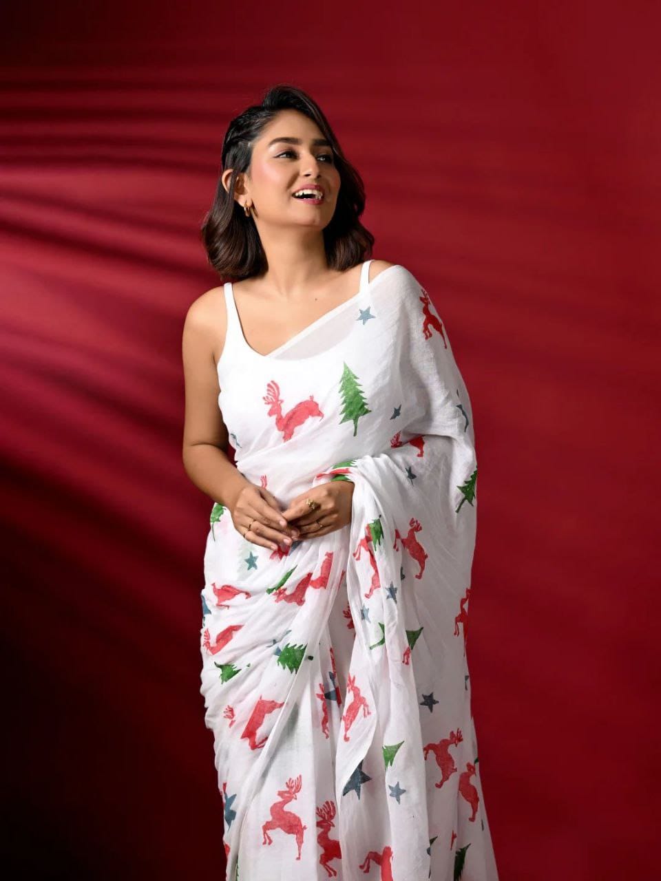 Woman wearing a white saree with colorful patterns against a red background