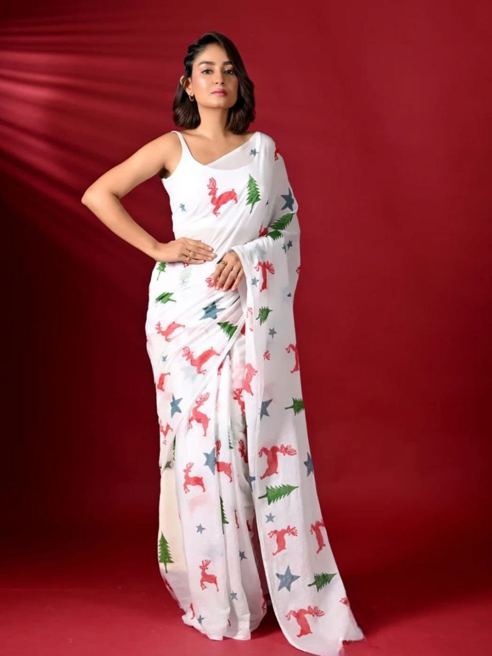 Woman wearing a white saree with colorful patterns against a red background