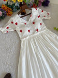 White dress with red heart patterns on a hanger against a floral background