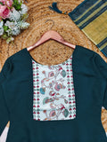 Green dress with floral pocket on a hanger, surrounded by flowers and a woven mat.