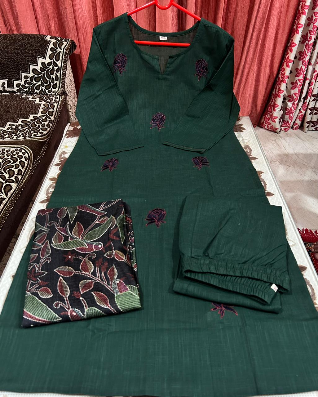 Green embroidered outfit with a matching scarf on a bed