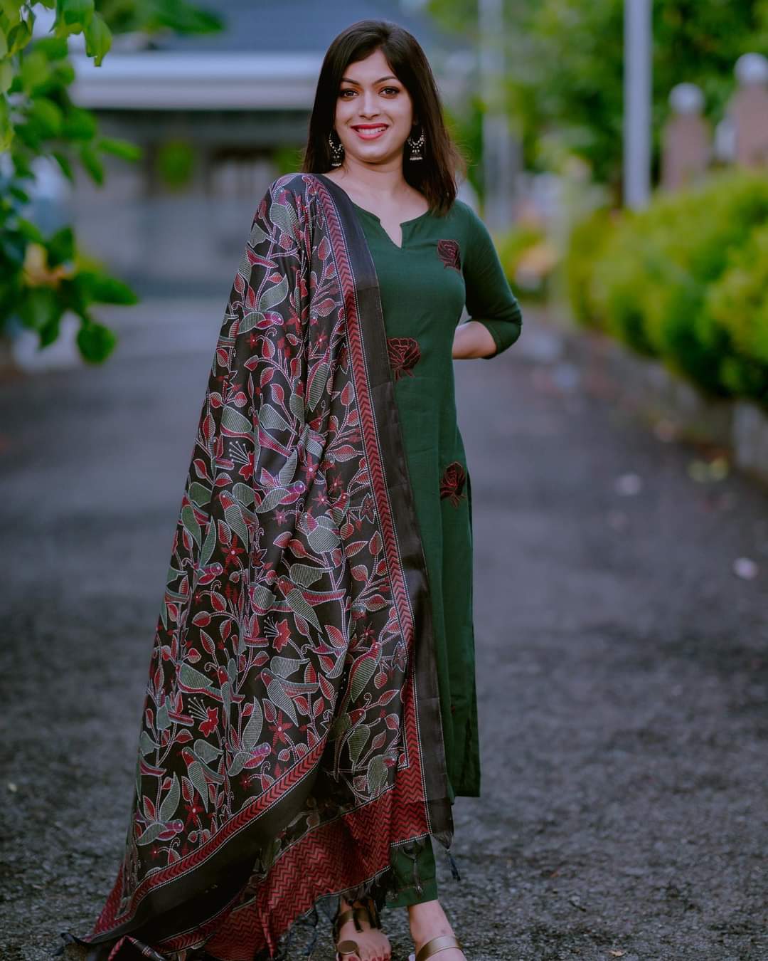 Woman in a green dress with a patterned shawl standing outdoors.
