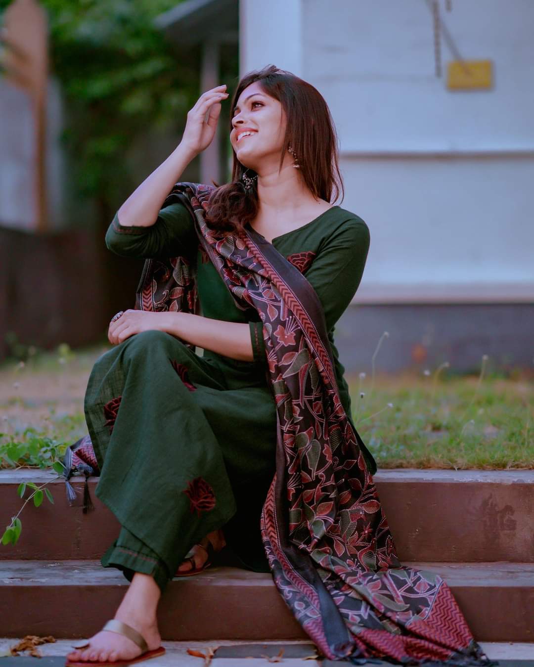 Woman in a green dress with a patterned shawl standing outdoors.