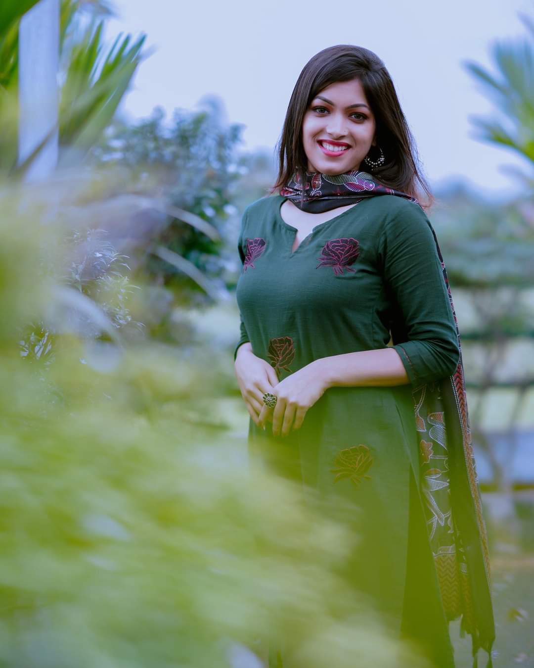 Woman in a green traditional outfit standing outdoors with blurred greenery in the background