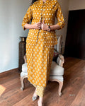 Person wearing a mustard yellow traditional outfit with white patterns in a room.