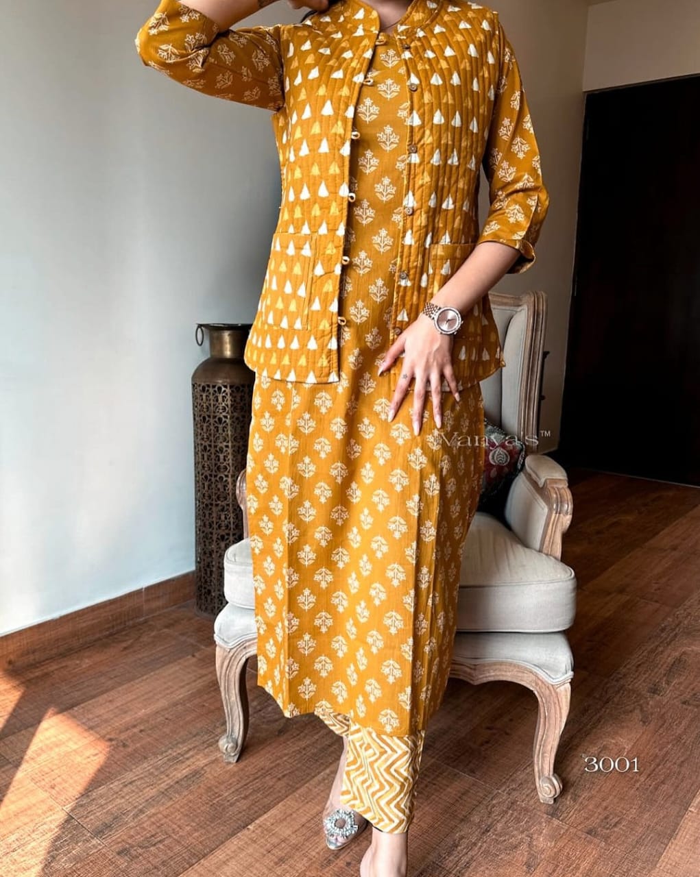 Person wearing a mustard yellow traditional outfit with white patterns in a room.
