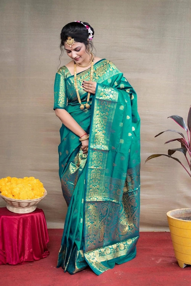 Woman in a green saree with gold patterns standing indoors.
