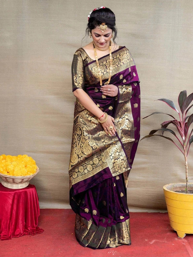 Woman in a green saree with gold patterns standing indoors.