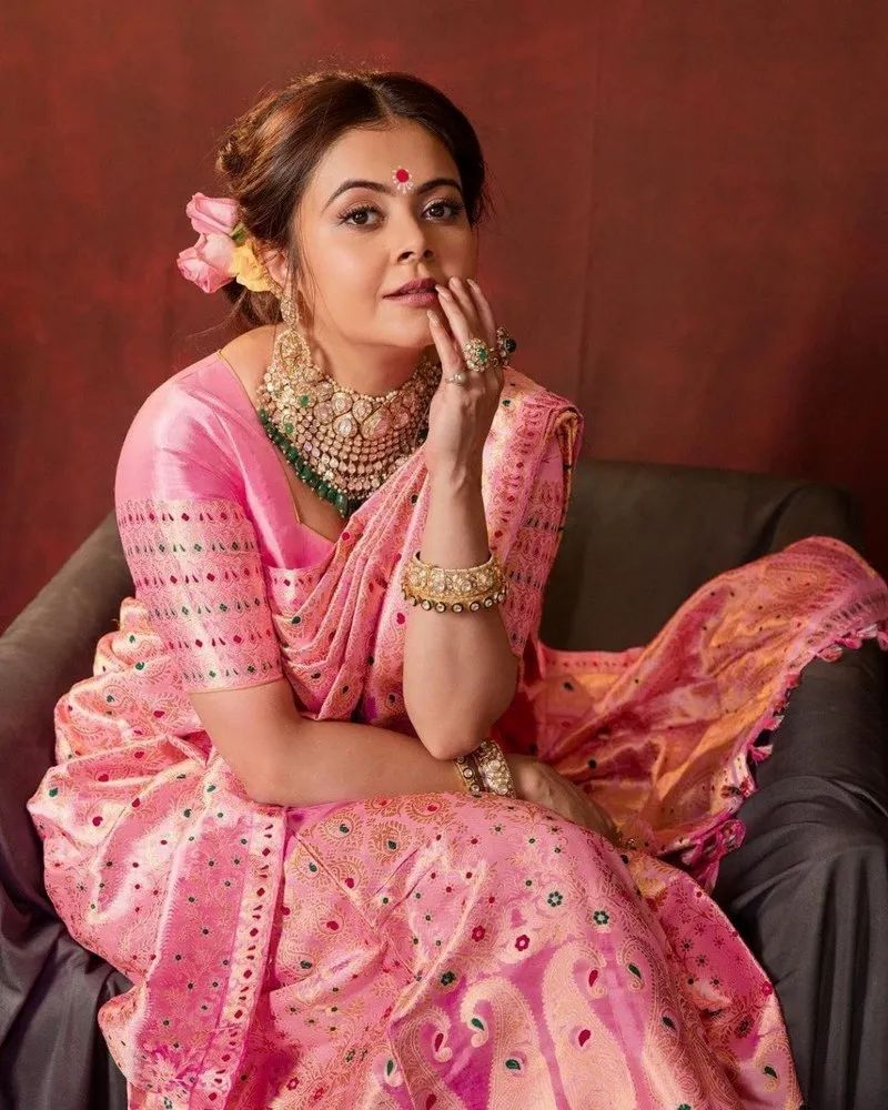 Woman in a pink saree with jewelry against a brown background